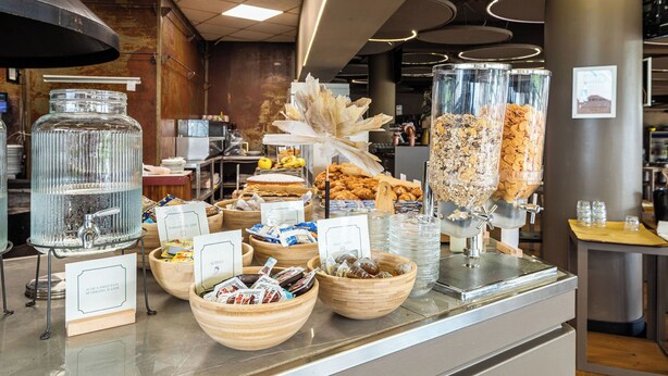 A buffet counter with various food items and a water dispenser. - The Gate Hotel (Sesto Fiorentino)