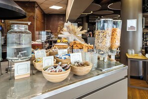 A buffet counter with various food items and a water dispenser. - The Gate Hotel (Sesto Fiorentino)