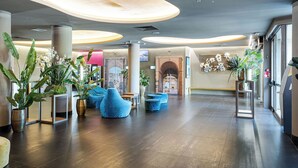A spacious lobby with modern furniture, large potted plants, and a view of the city through a glass wall. - The Gate Hotel (Sesto Fiorentino)