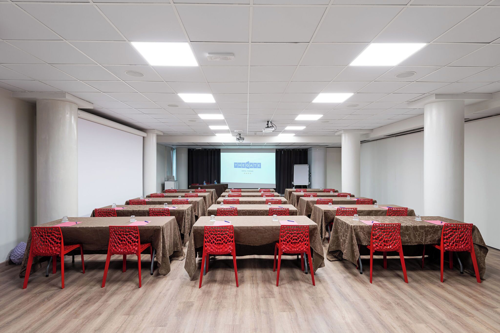 A conference room with multiple tables and chairs, a projector screen, and a presentation screen.