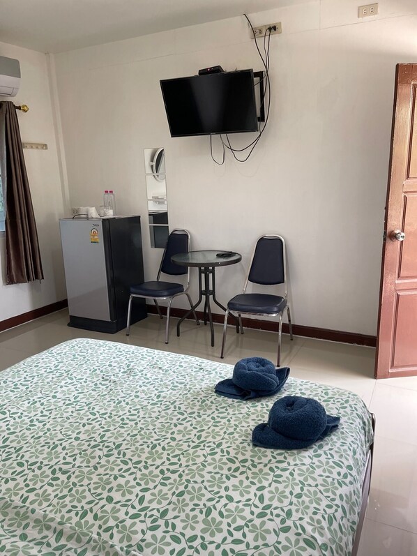 Une chambre d’hôtel comprenant un lit, deux chaises, une petite table, un téléviseur fixé au mur et un réfrigérateur.