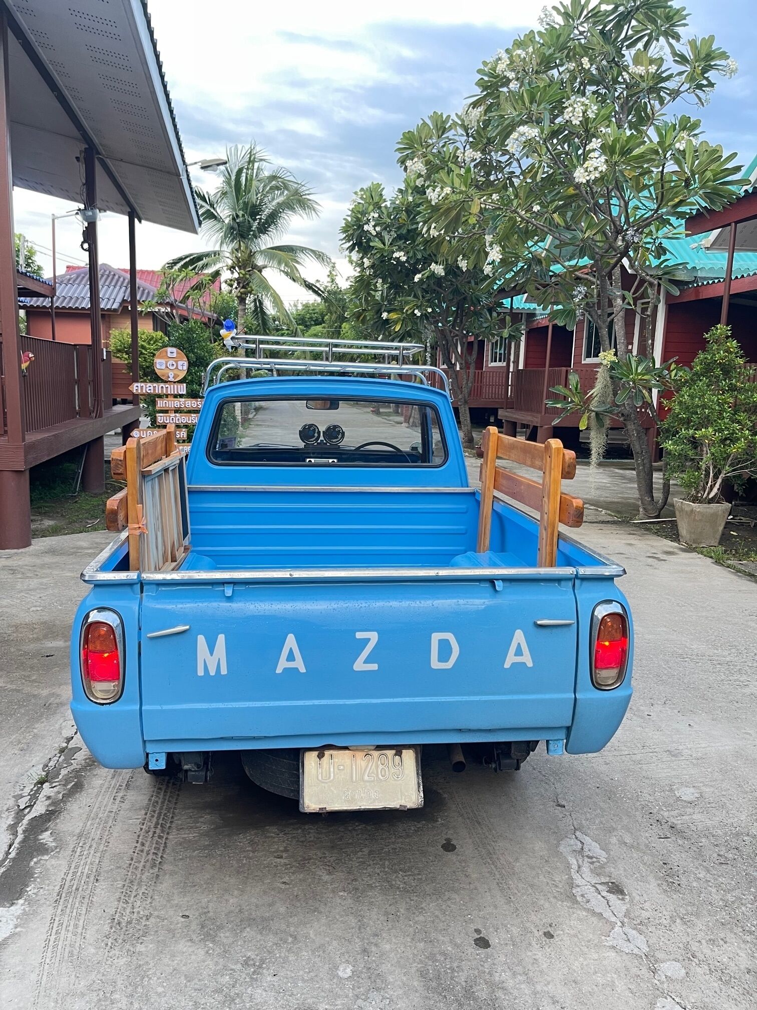 Ein blauer Mazda-Pick-up steht auf einem Einfahrt mit einer hölzernen Sitzbank im Laderaum.