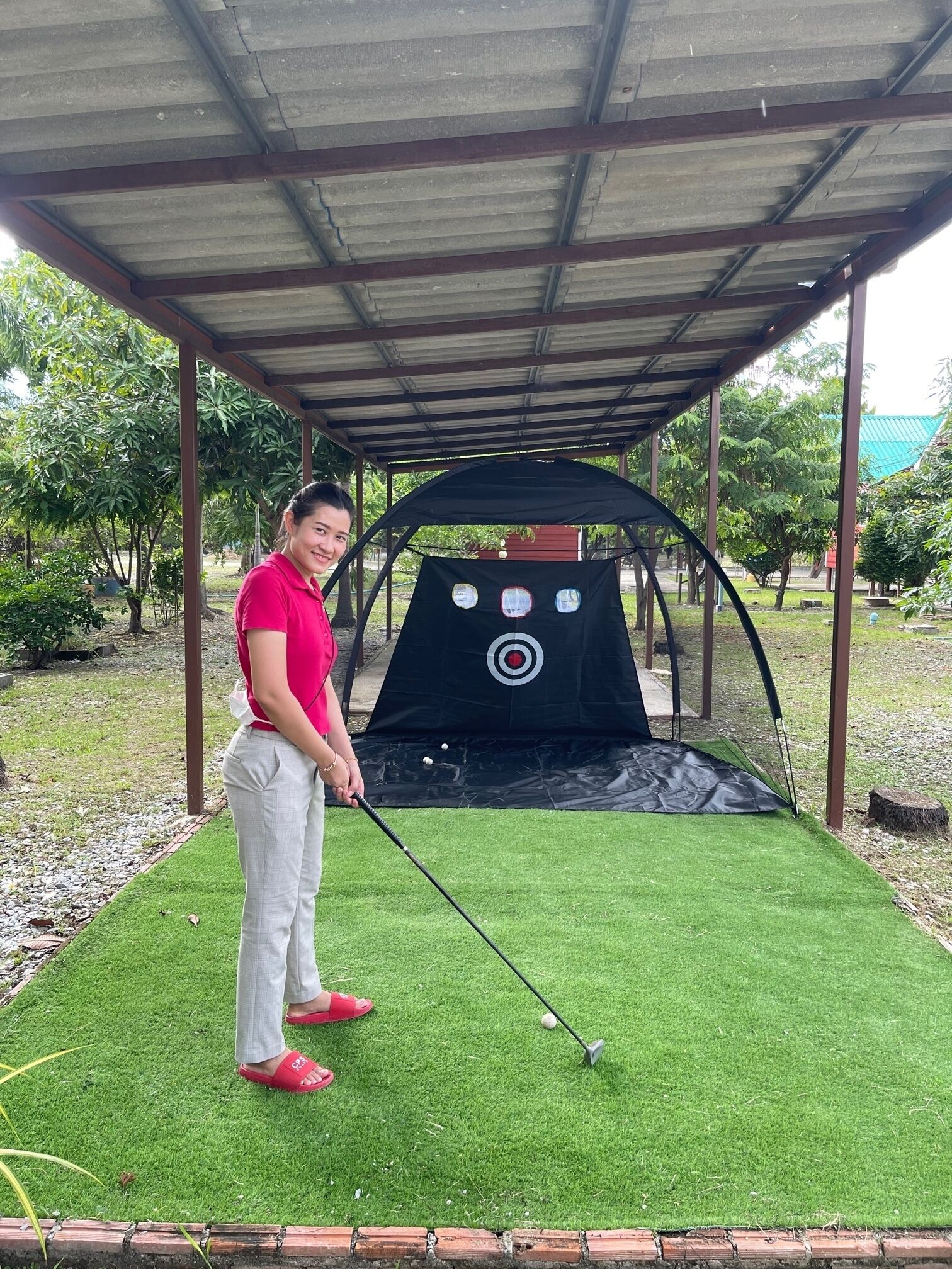 Una persona jugando golf bajo una estructura cubierta, con un objetivo al fondo.