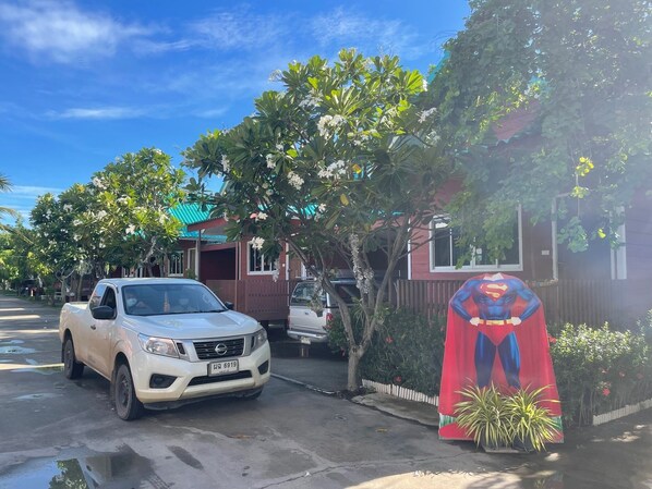 Un camionnette blanche est garée dans une rue, avec une statue de Superman et une maison au toit rouge en arrière-plan.