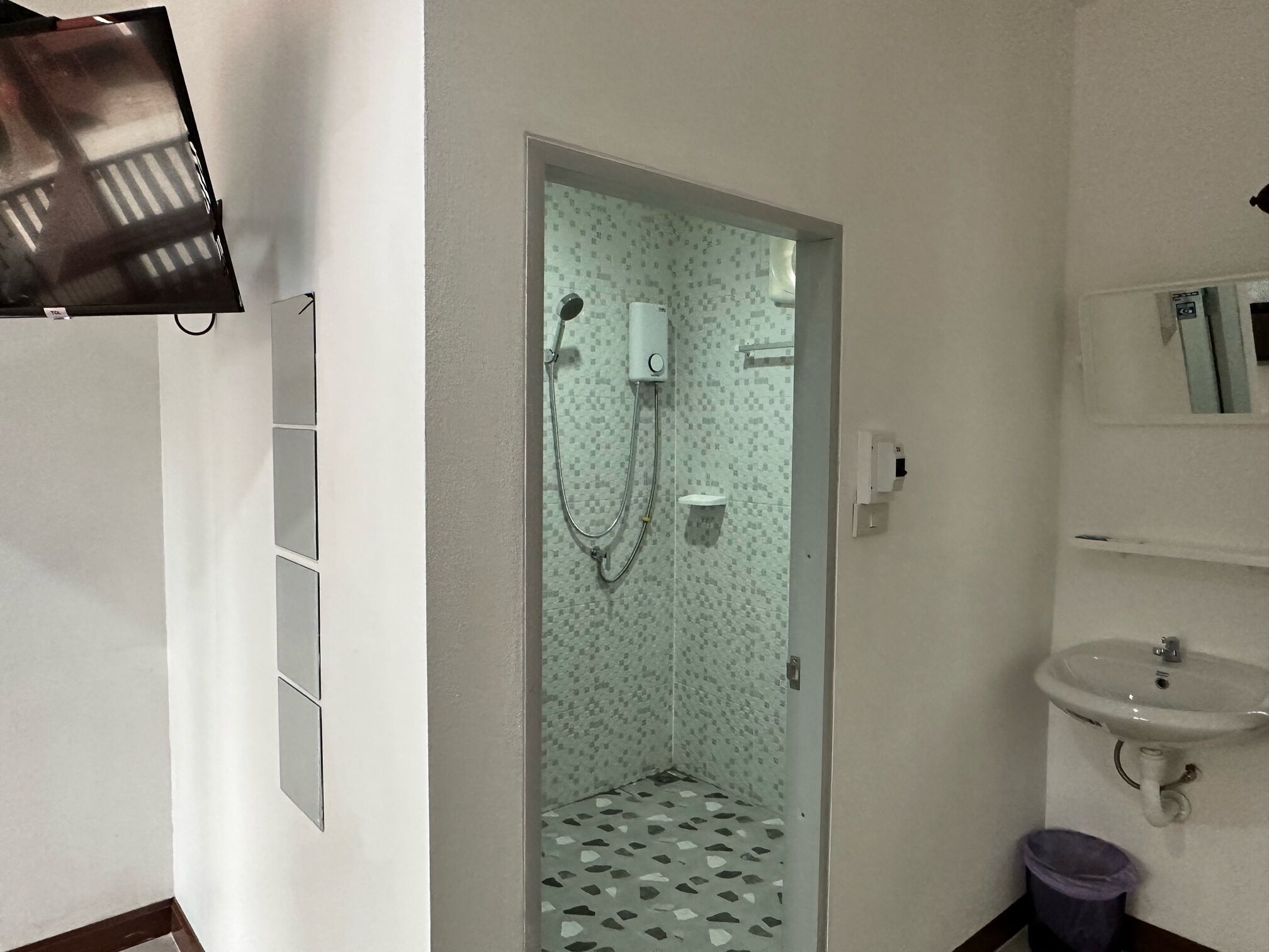 Een badkamer met een douche, wastafel en spiegel.
