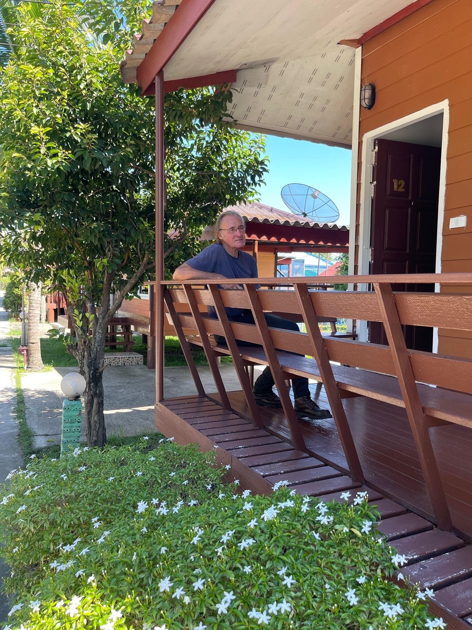 A man sitting on a wooden bench outside a building with a number 12 door.