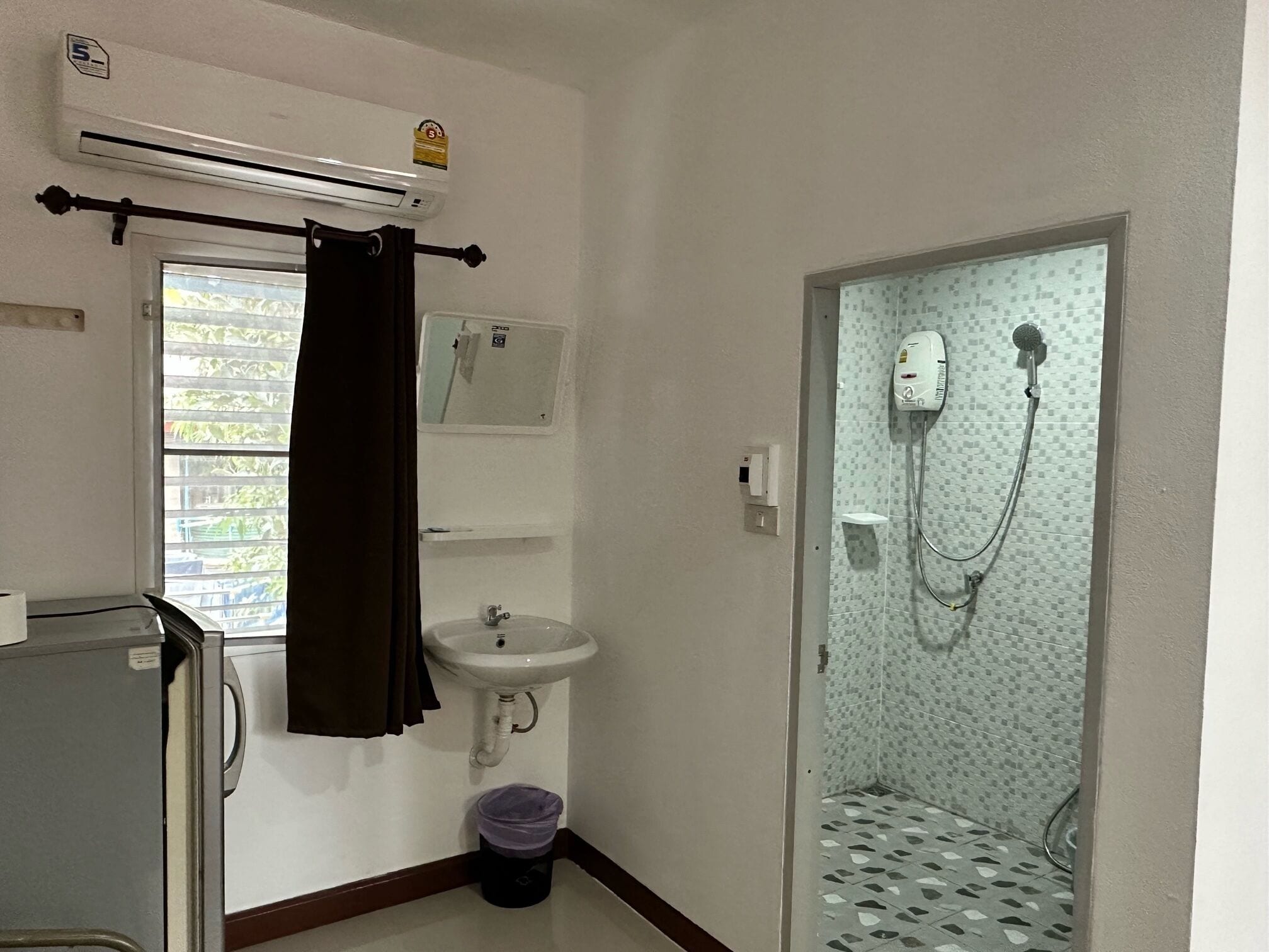 A small bathroom with a sink, a shower, and a window with blinds.