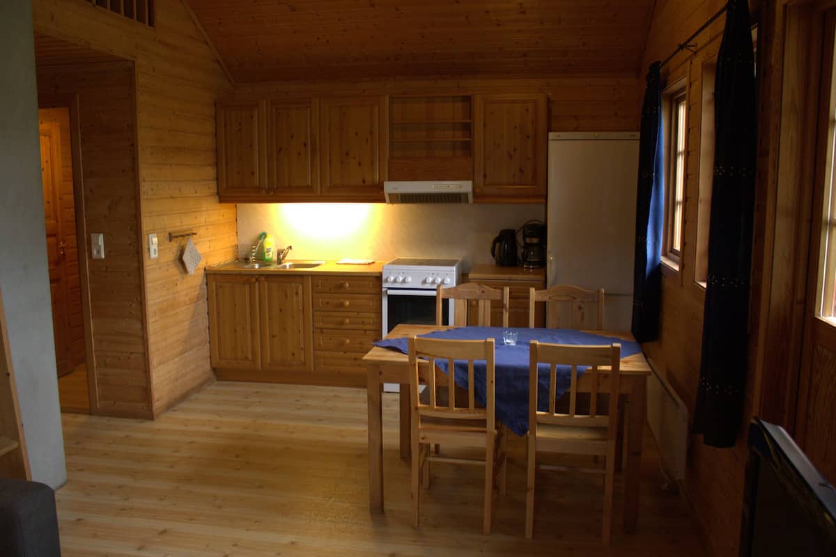 A wooden cabin interior with a kitchen area, dining table, and chairs.