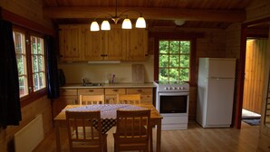 A wooden cabin kitchen with a dining table, chairs, a stove, and a refrigerator. - Sjøholt Camping (Ålesund)
