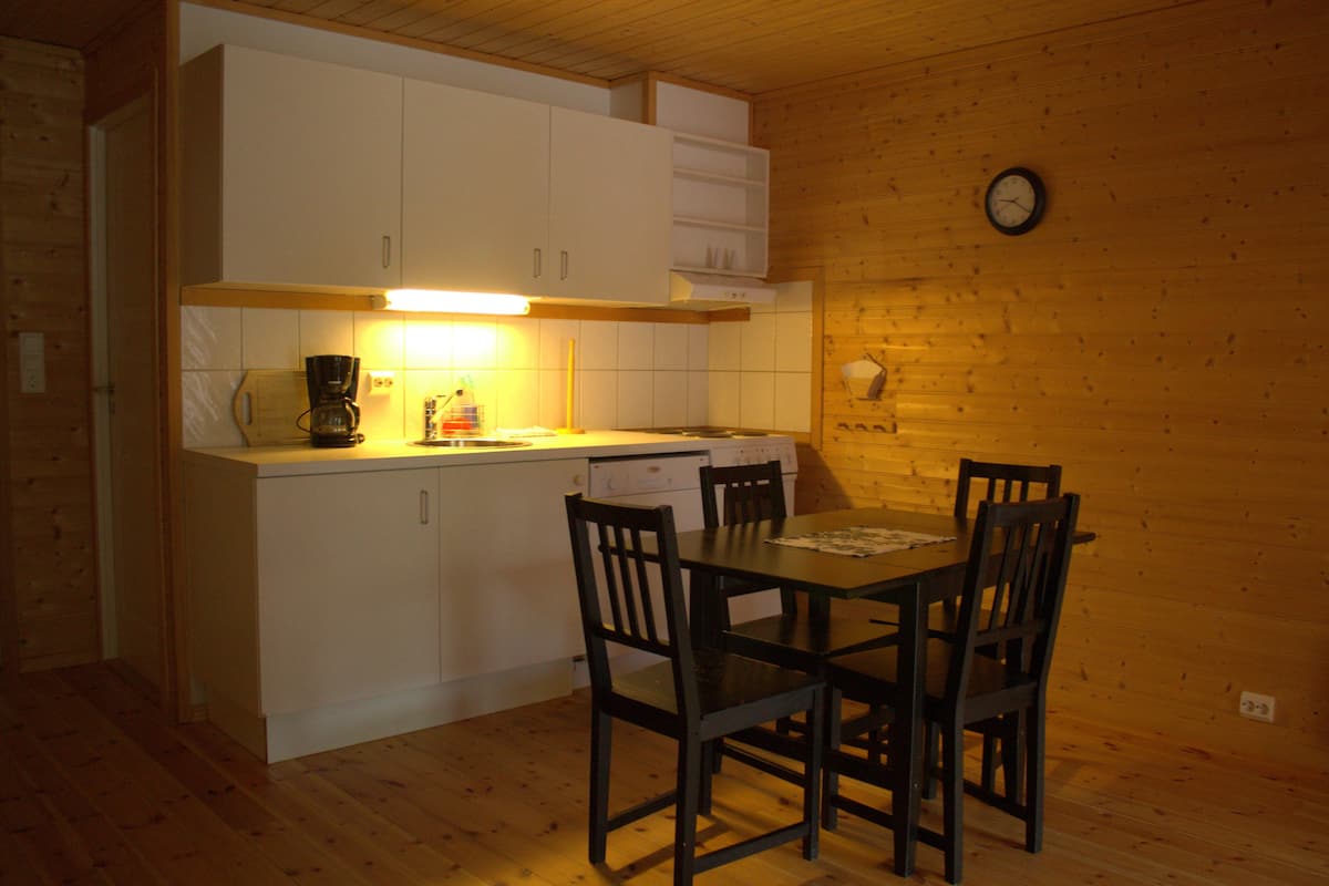 A compact kitchen with white cabinets, a wooden dining table with four chairs, and a clock on the wall.