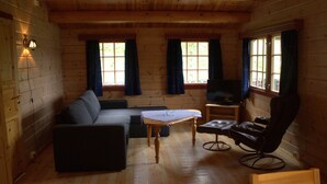 A log cabin interior with a sofa, a small table, a recliner, and a television. - Sjøholt Camping (Ålesund)