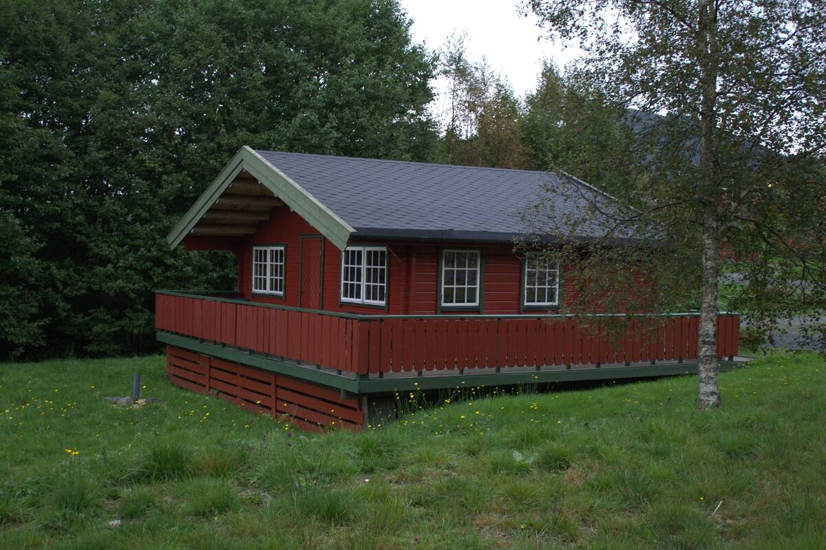 A red wooden cabin with a green porch, surrounded by grass and trees.