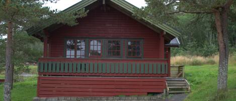 A red cabin with a porch, surrounded by trees.