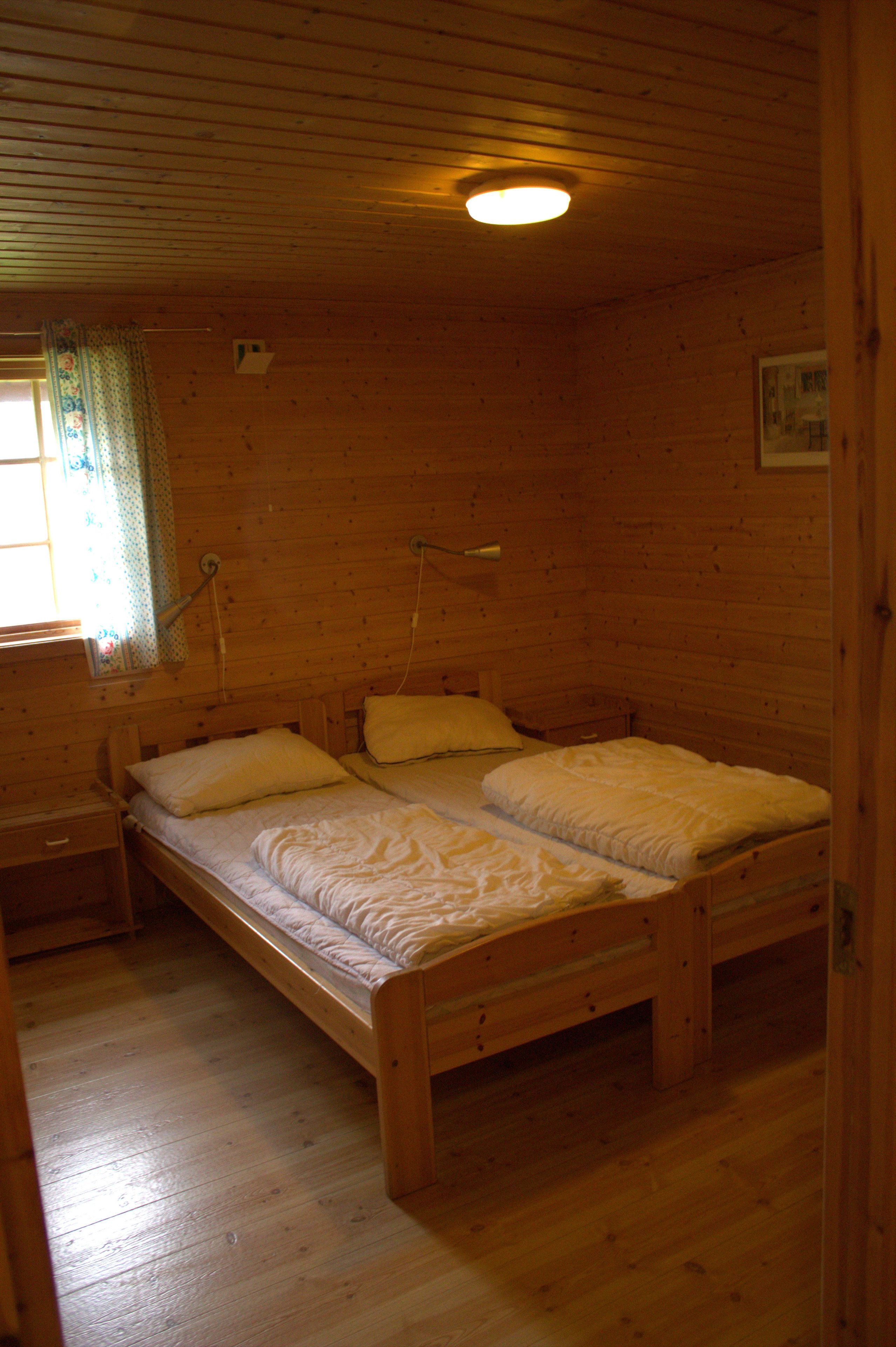 Camera da letto in una baita di legno con due letti singoli, un comodino, una finestra con tende e una lampada a soffitto.