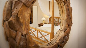 A bedroom with a wooden bed frame, a bedside table with a lamp, and a mirror with a wooden frame. - Troulakis Beach Hotel (Chania)