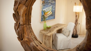 A rustic interior with a wooden table, a white chair, a painting of a boat on water, and a lamp. - Troulakis Beach Hotel (Chania)