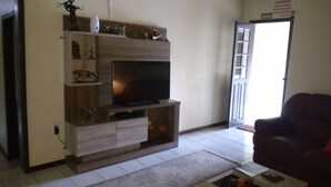 A living room with a TV on a wooden entertainment unit, a sofa, and a door with a sign. - Hospedaria Ondas do Rosa (Garopaba)