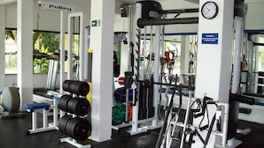 A gym with weightlifting equipment, a clock, and a sign indicating attention to safety. - Hospedaria Ondas do Rosa (Garopaba)