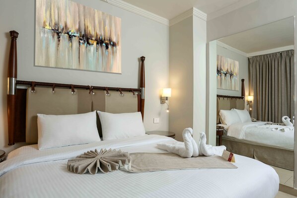 Quarto de hotel com uma cama grande, cabeceira, mesa de cabeceira, abajur e obras de arte na parede.