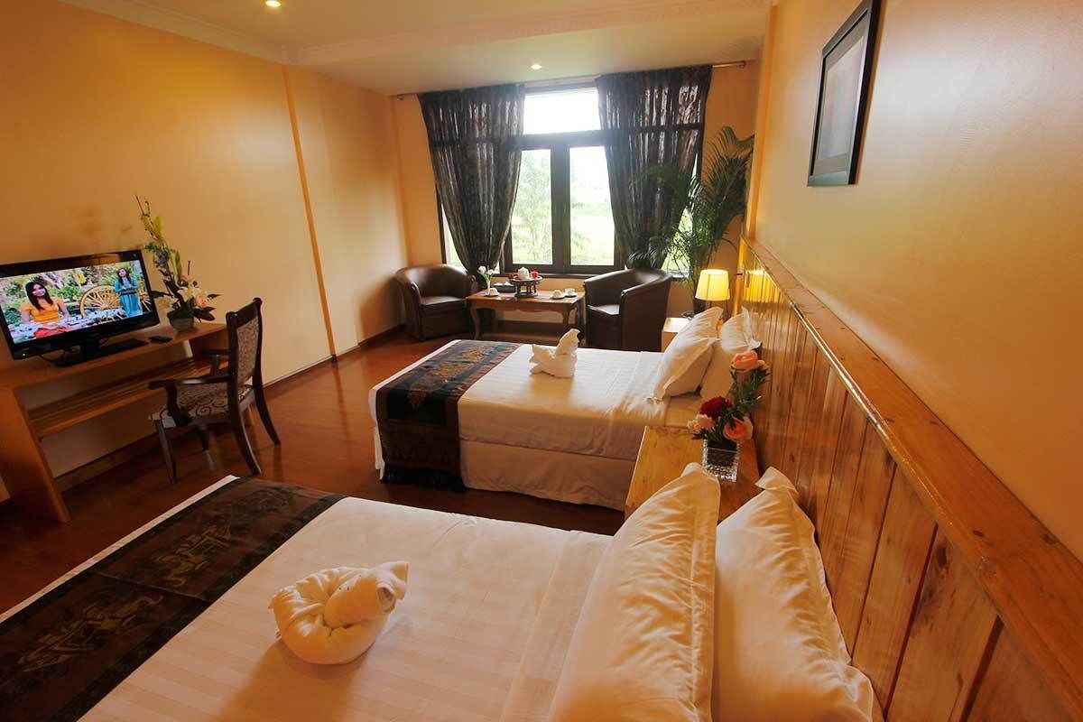 A hotel room with two beds, a TV, a desk, and a window with curtains.