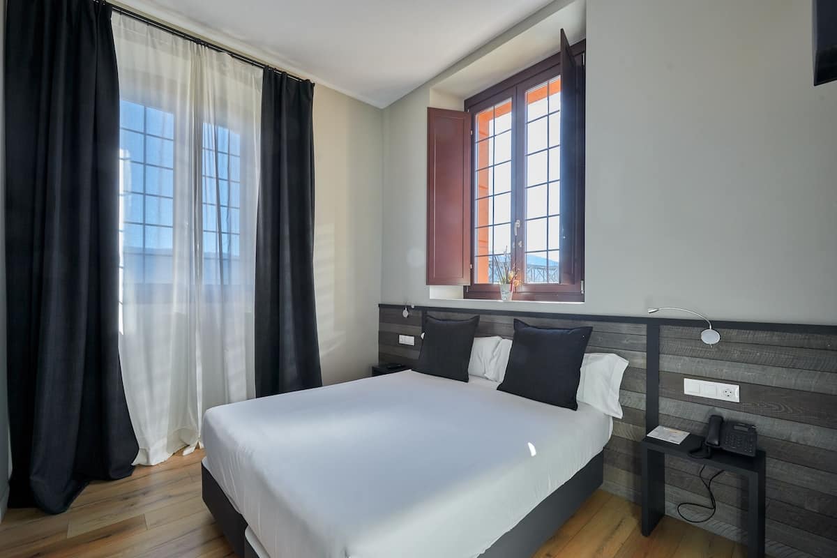 A modern hotel room with a large bed, a bedside table with a phone, and a window with curtains.