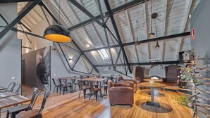 A spacious loft-style room with high ceilings, exposed beams, and a sloped ceiling. There are multiple seating areas with tables and chairs, and a decorative birdhouse on a wall. - Hotel Parada Puigcerdà (Puigcerda)