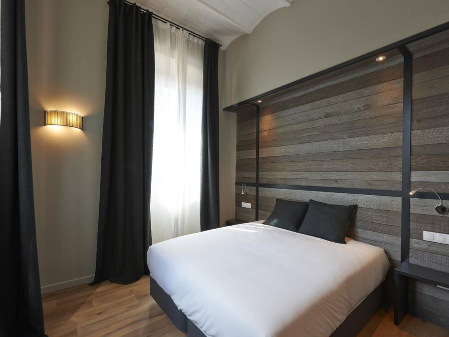 Une chambre à coucher moderne avec une tête de lit en bois, un grand lit avec une literie blanche et un luminaire fixé au mur.