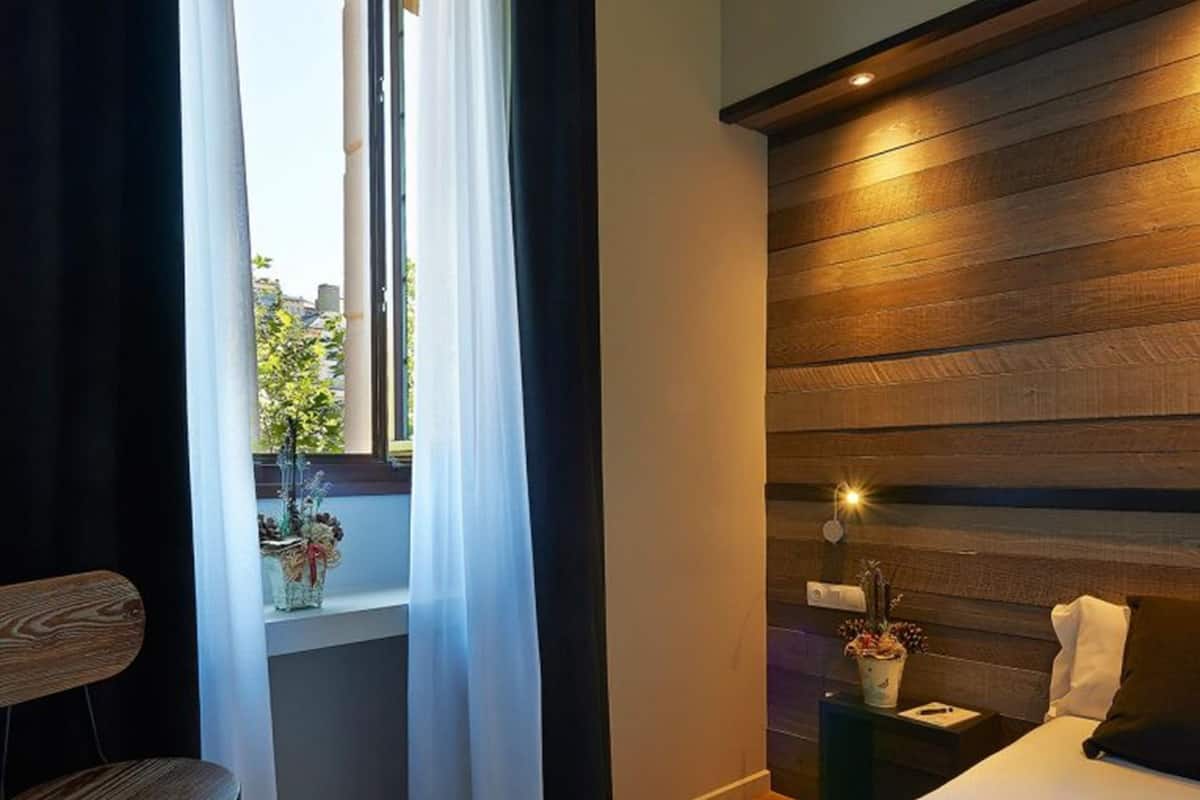 A bedroom with a wooden headboard, a bed, a nightstand, a chair, and a window with curtains.