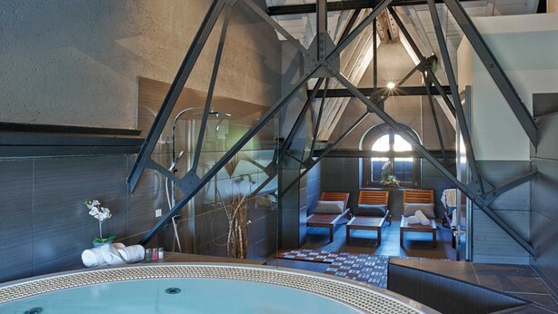 A modern spa area with a large hot tub, seating area with loungers, and a visible staircase. - Hotel Parada Puigcerdà (Puigcerda)