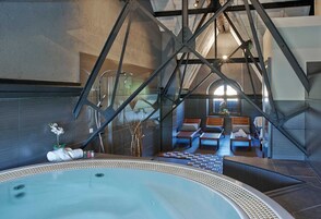 Un área de spa moderna con un jacuzzi grande, zona de estar con tumbonas y una escalera visible.