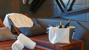 A wooden lounge chair with a towel, a bucket with champagne bottles, and a cushion on a wooden table in a modern interior. - Hotel Parada Puigcerdà (Puigcerda)