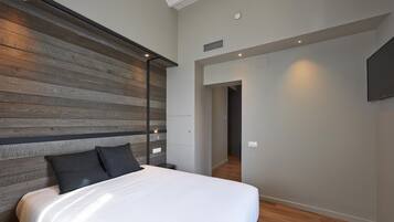A bedroom with a wooden headboard, a bed with white bedding, and a flat-screen TV mounted on the wall.