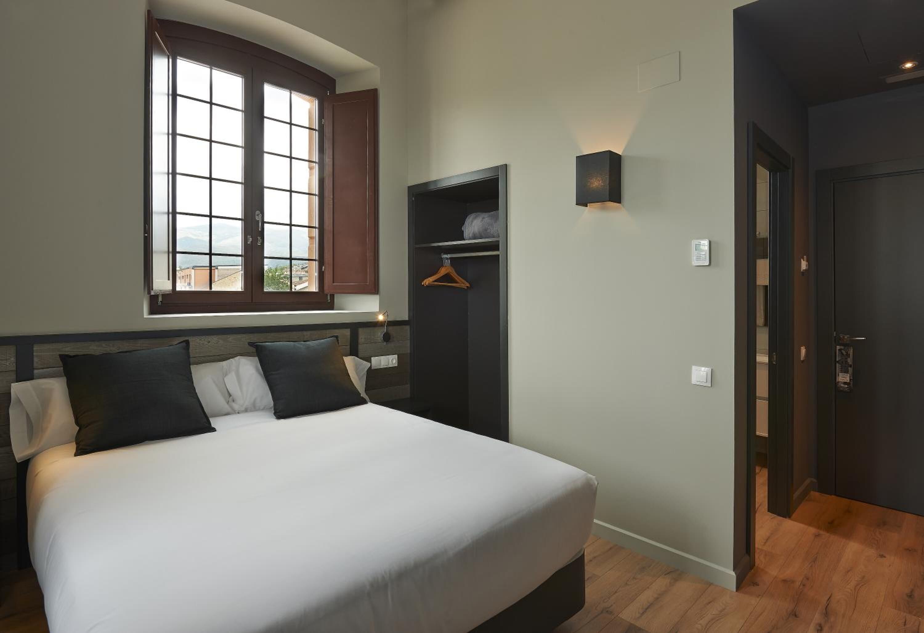 A bedroom with a large bed, a wardrobe, a window with a view, and a door.