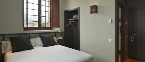 A bedroom with a large bed, a wardrobe, a window with a view, and a door.