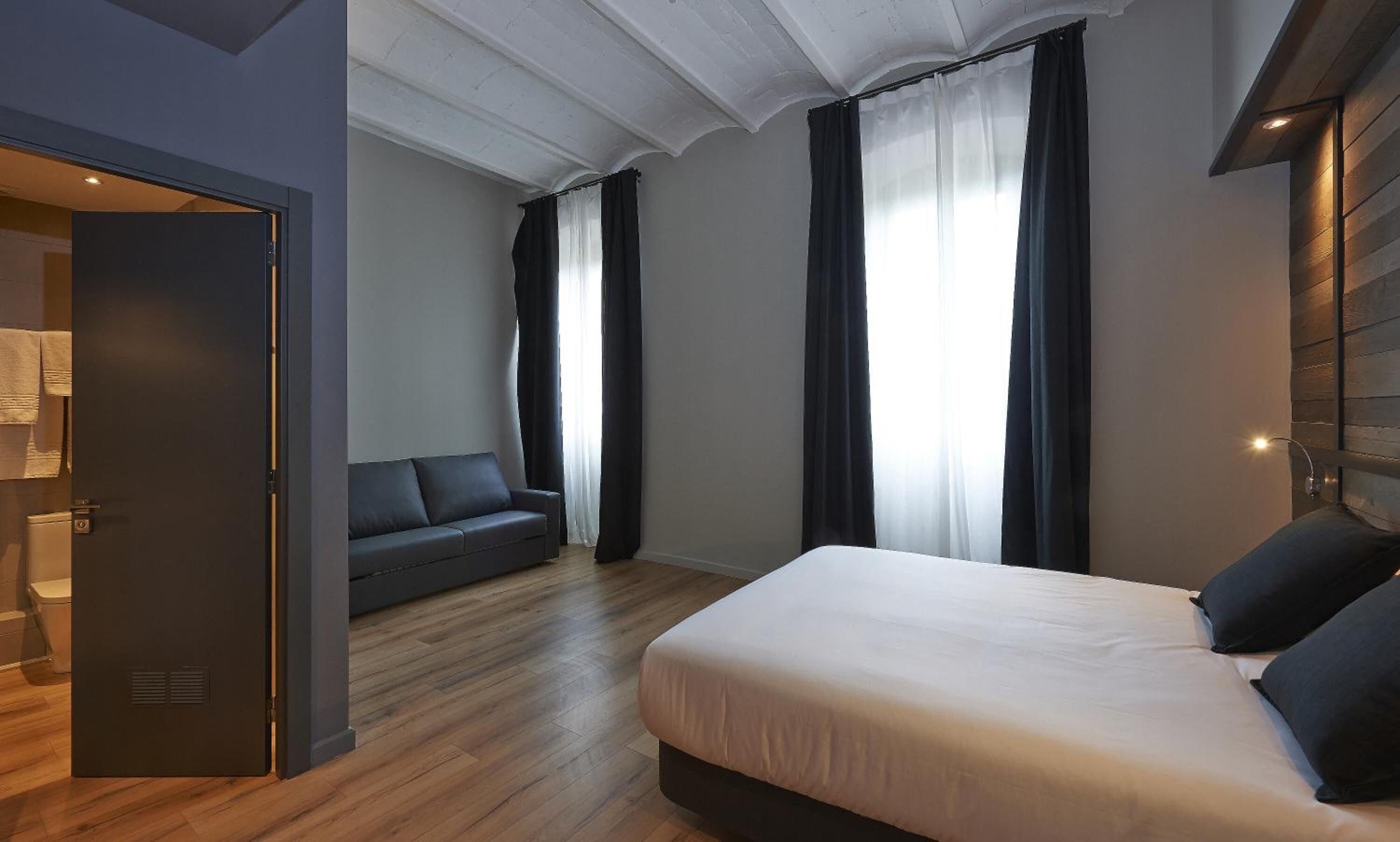 A modern hotel room with a bed, a sofa, and a bathroom.