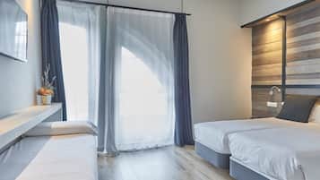 A modern bedroom with two beds, a wooden accent wall, a bedside table with a vase, and sheer curtains allowing natural light.