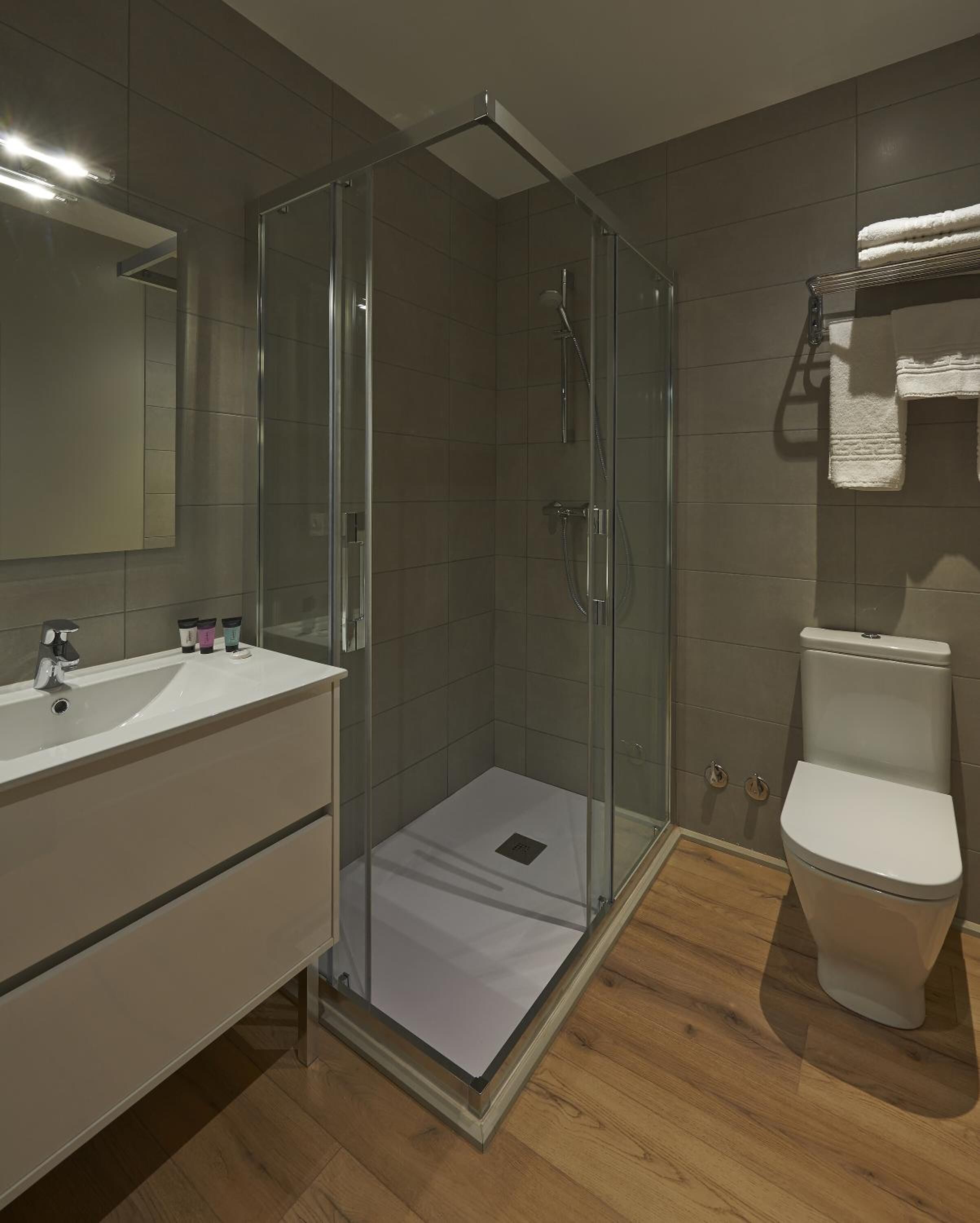 Un baño moderno con ducha de vidrio, lavamanos blanco y un inodoro.