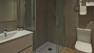 Un baño moderno con ducha de vidrio, lavamanos blanco y un inodoro.