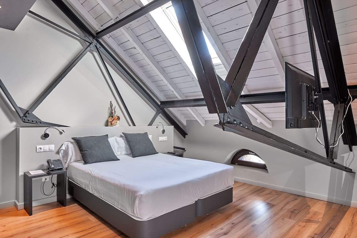A modern loft bedroom with a sloped ceiling, a bed, a nightstand, and a mounted TV.