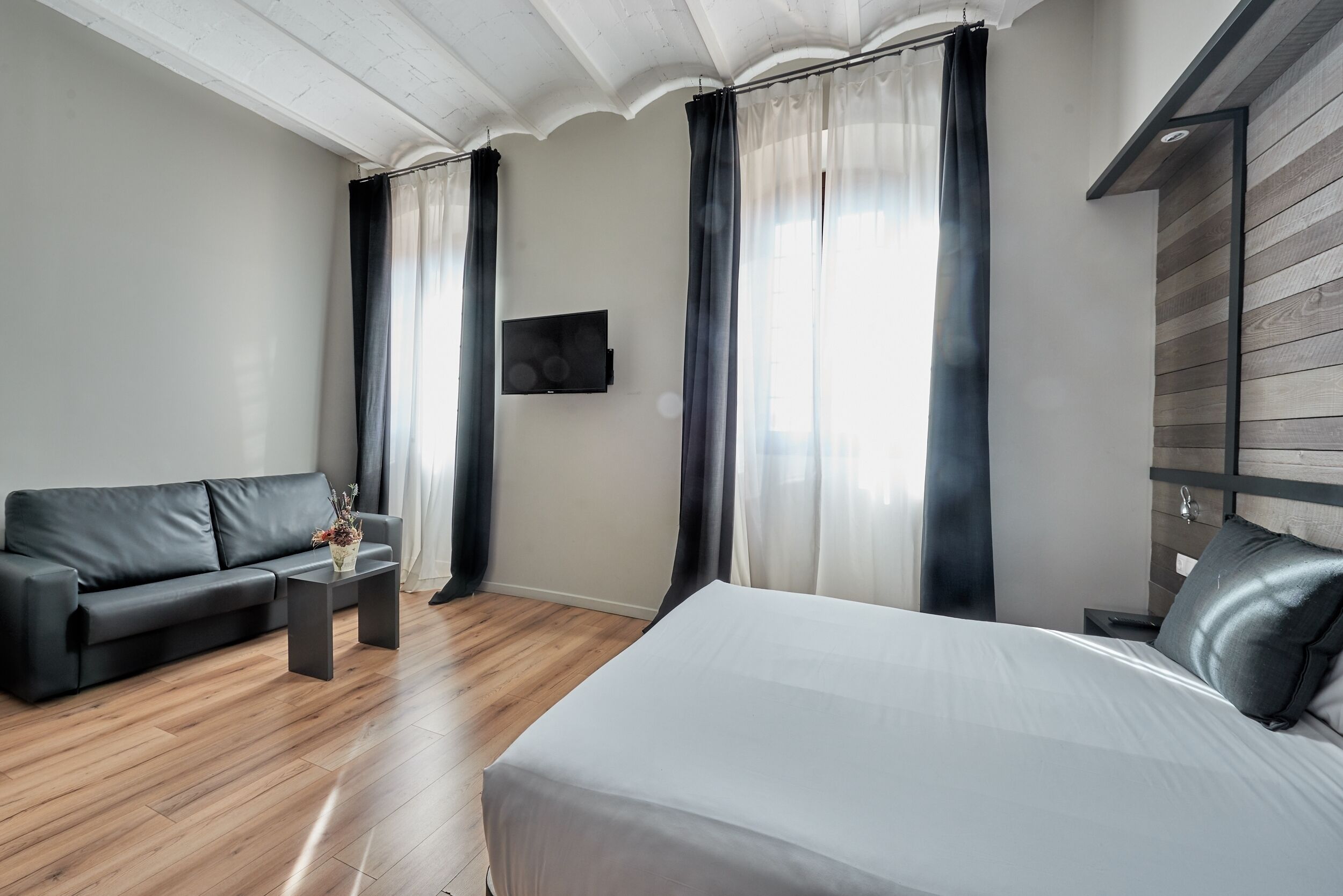 Una habitación de hotel moderna con una cama grande, un sofá, una mesita y un televisor montado en la pared.