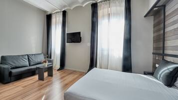Una habitación de hotel moderna con una cama grande, un sofá, una mesita y un televisor montado en la pared.