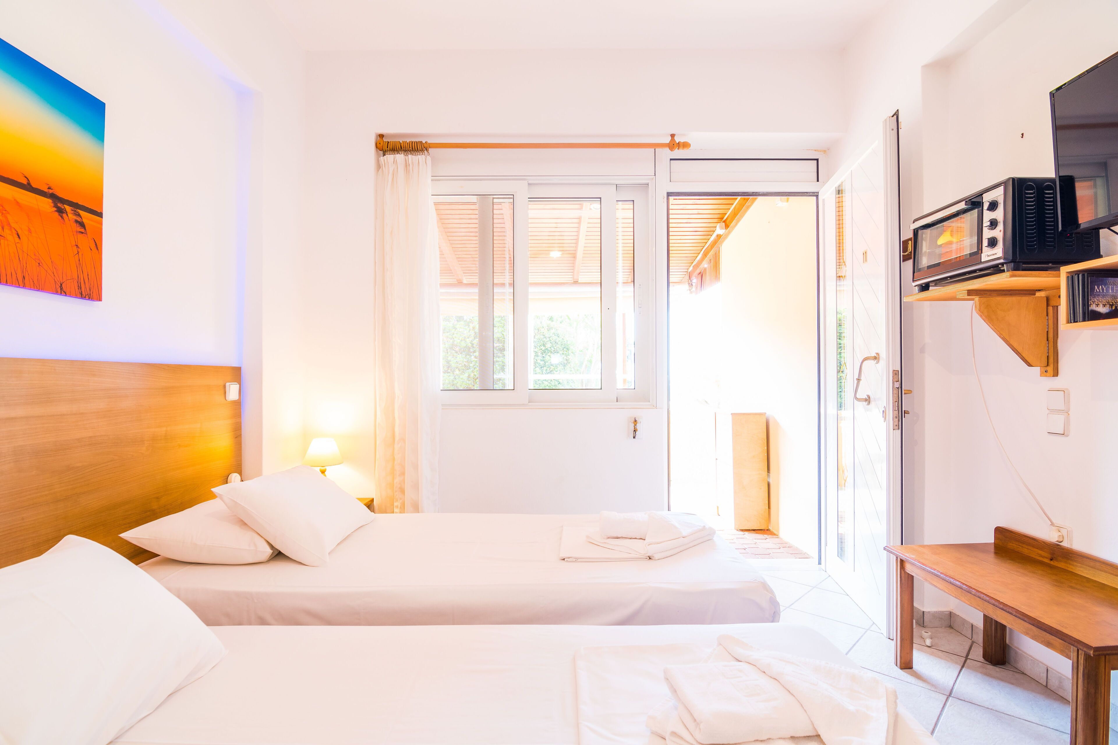 A hotel room with two beds, a wooden headboard, a painting, a microwave, and a sliding glass door to the outside.
