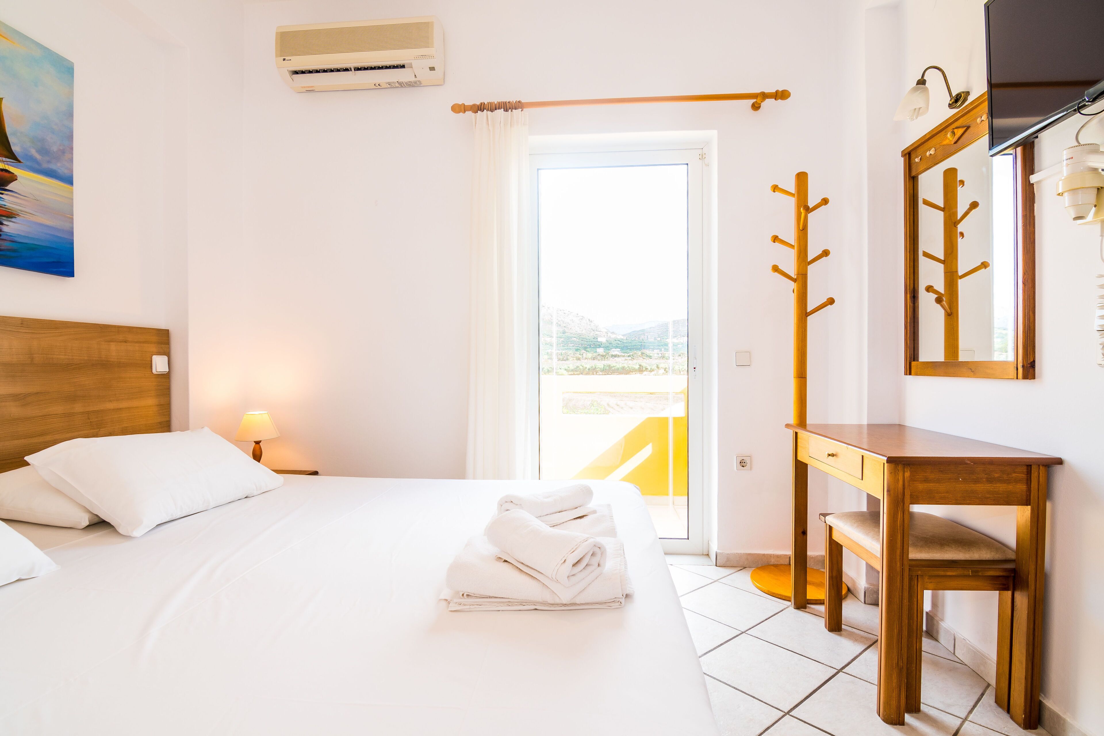Habitación de hotel con una cama, una mesita de noche de madera, un escritorio, un espejo y vistas al exterior.