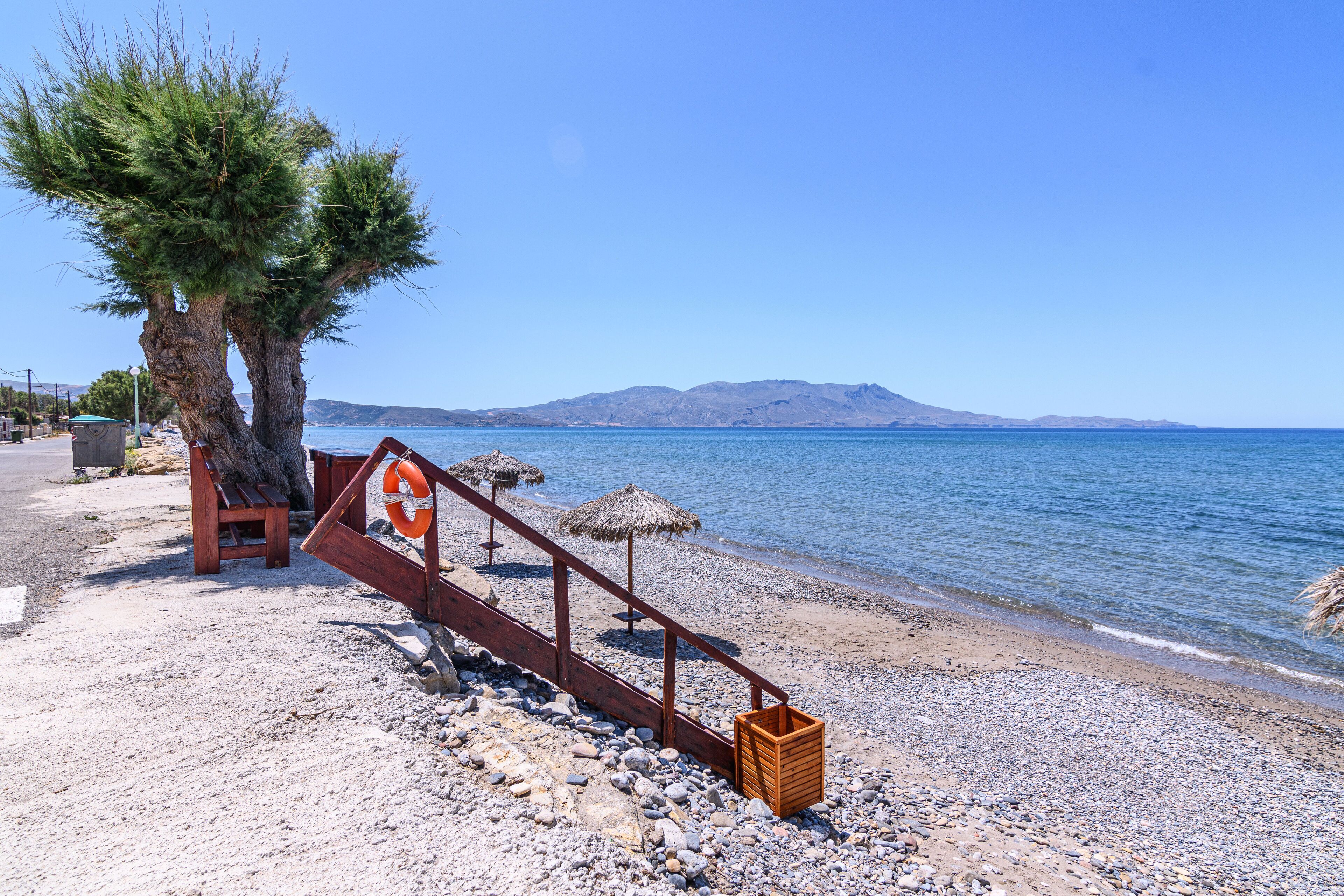 A beach with a wooden walkway, a lifebuoy, and a thatched umbrella.