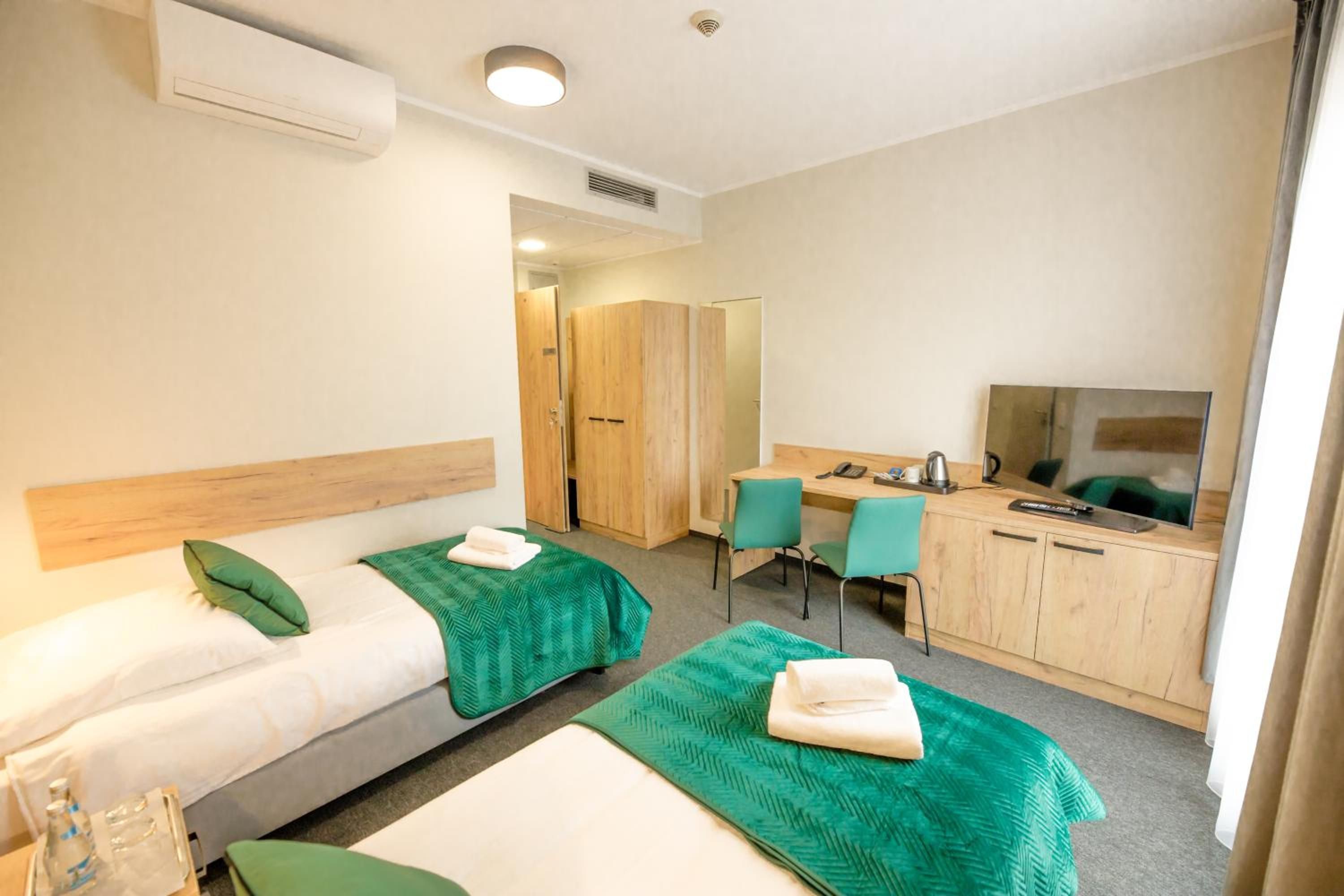 Una habitación de hotel con dos camas individuales, un escritorio con una silla, un televisor y un armario.