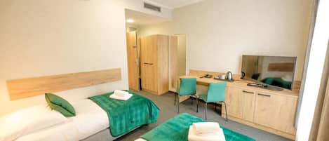 Quarto de hotel com duas camas de solteiro, uma escrivaninha com cadeira, televisão e armário.