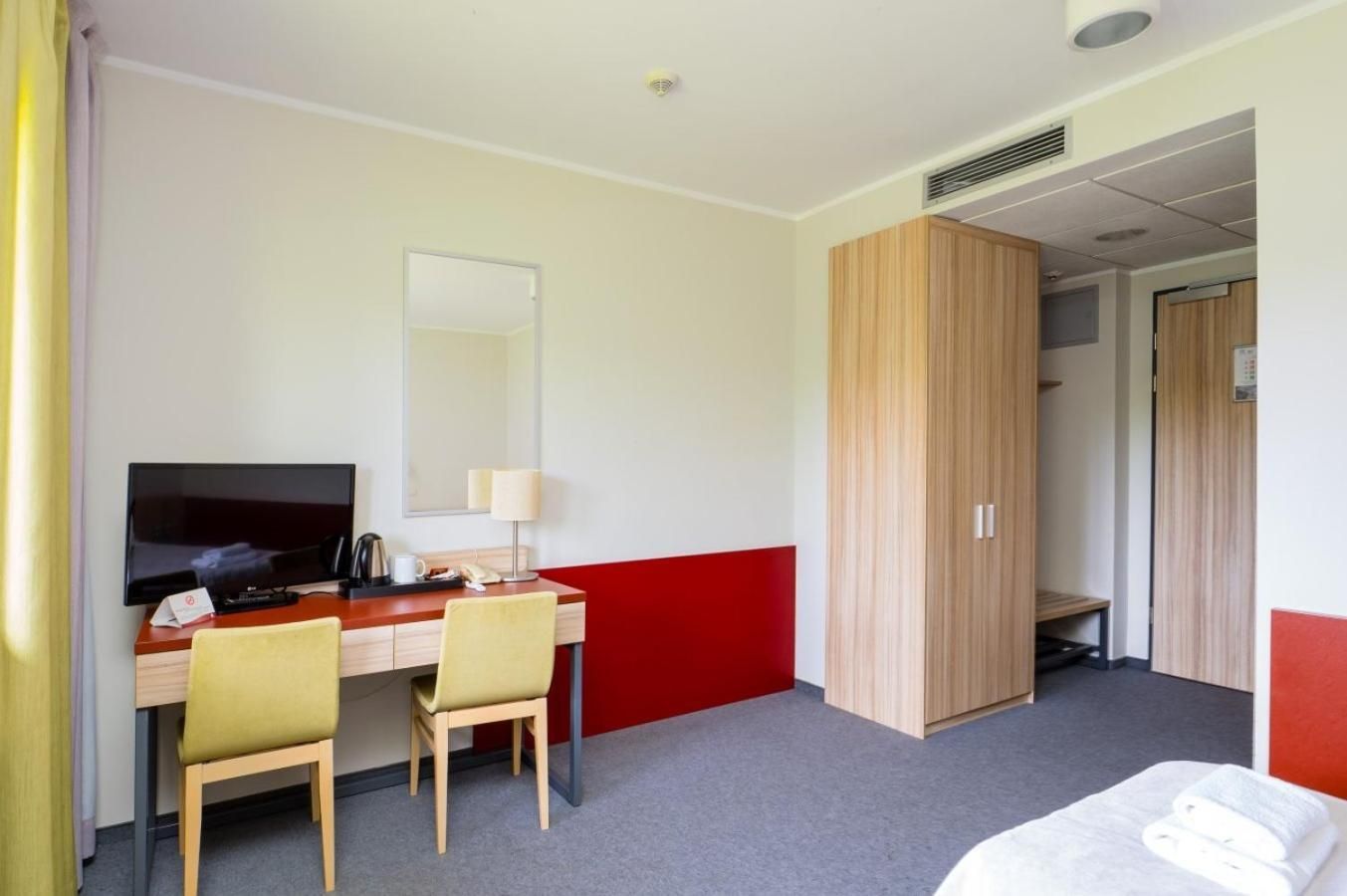 Una habitación de hotel con escritorio, sillas, televisor, espejo, armario y cama.