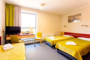 A hotel room with two beds, a desk with a television, a chair, and a window with curtains.
