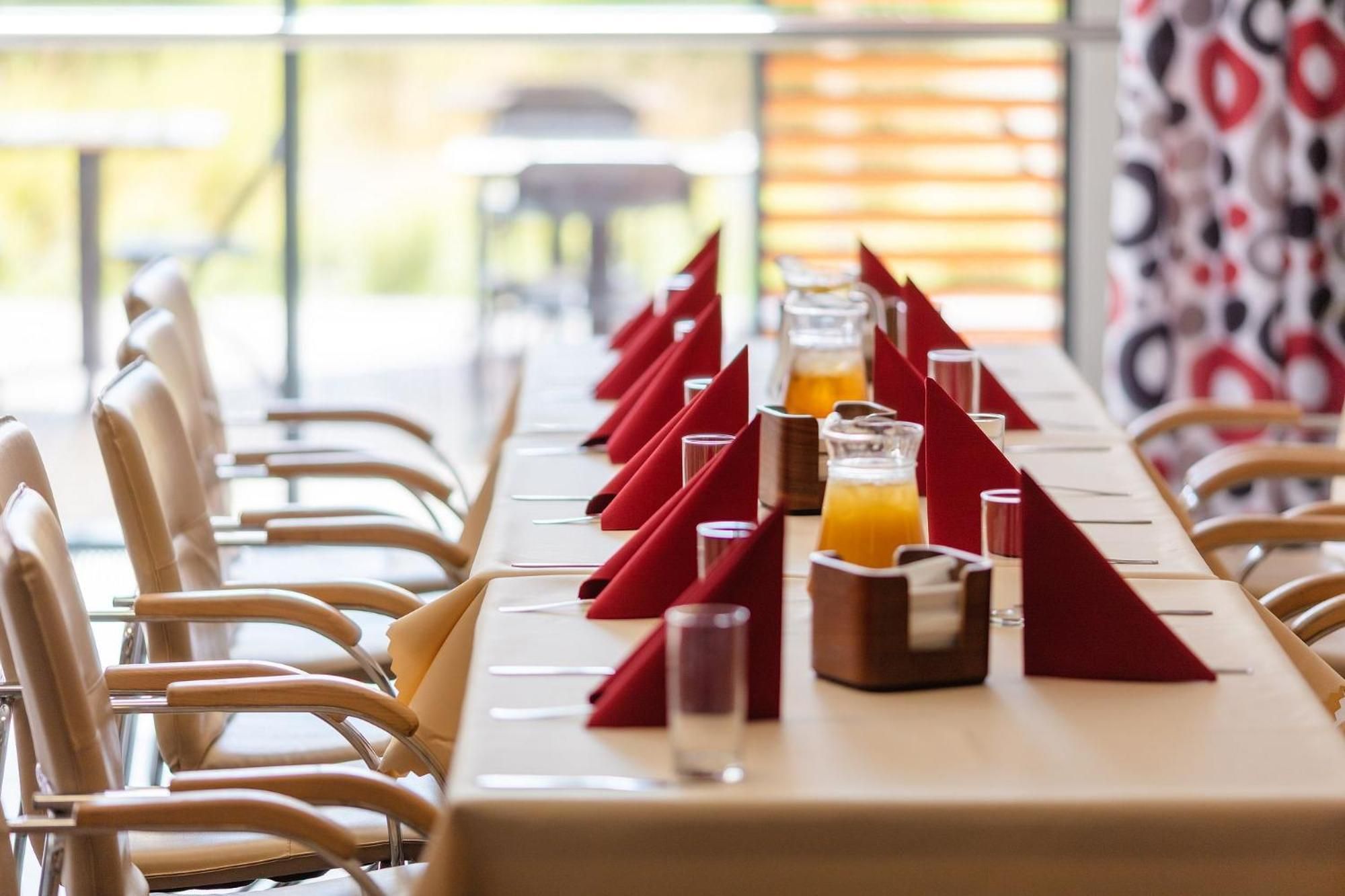 A long dining table with red napkins, glasses, and a bottle of orange juice.