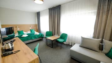 A hotel room with a bed, a desk with a kettle, a sofa, and a chair.